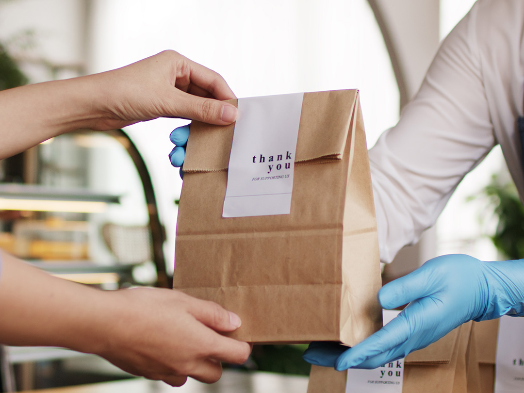 Cameriere con camicia bianca e guanti blu consegna una busta per asporto a un cliente